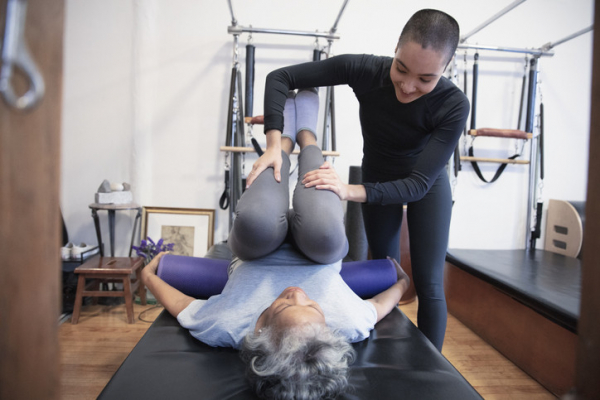 Trainer assisting older woman in a stretch